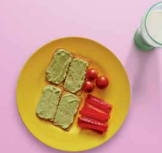 Avocado on melba toast with cherry tomatoes and red pepper sticks on a plate with a glass of milk on the side