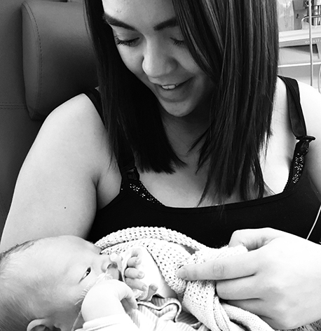 Black and white image of mother holding baby in her arms, looking down and smiling 