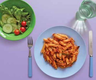 Image of tuna pasta on a plate with a side salad and glass of water.