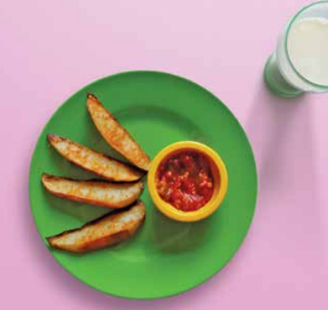 Potato wedges on a plate with a pot of tomato salsa and a glass of milk on the side