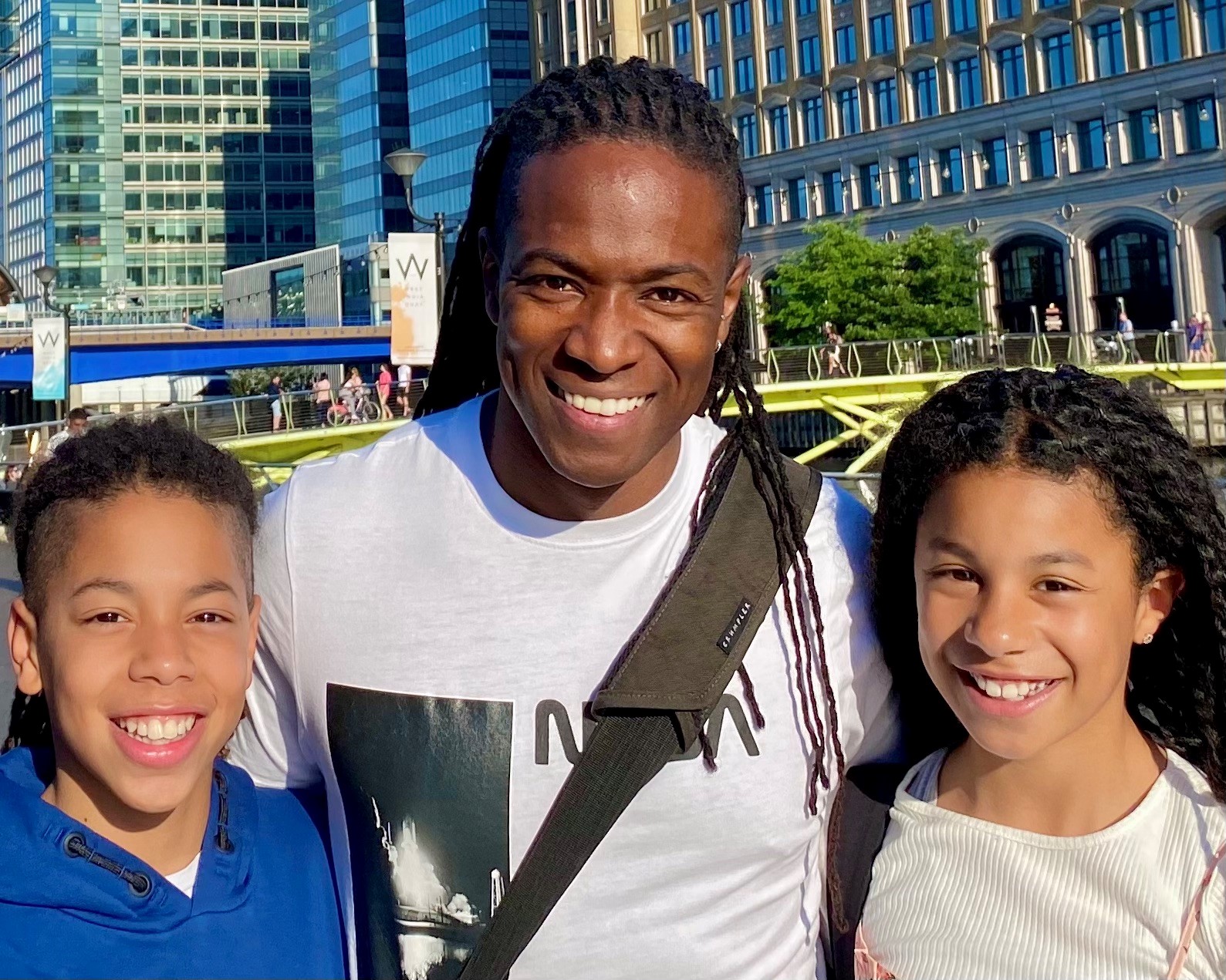 Image of Nigel standing with his two children, smiling and looking at the camera.