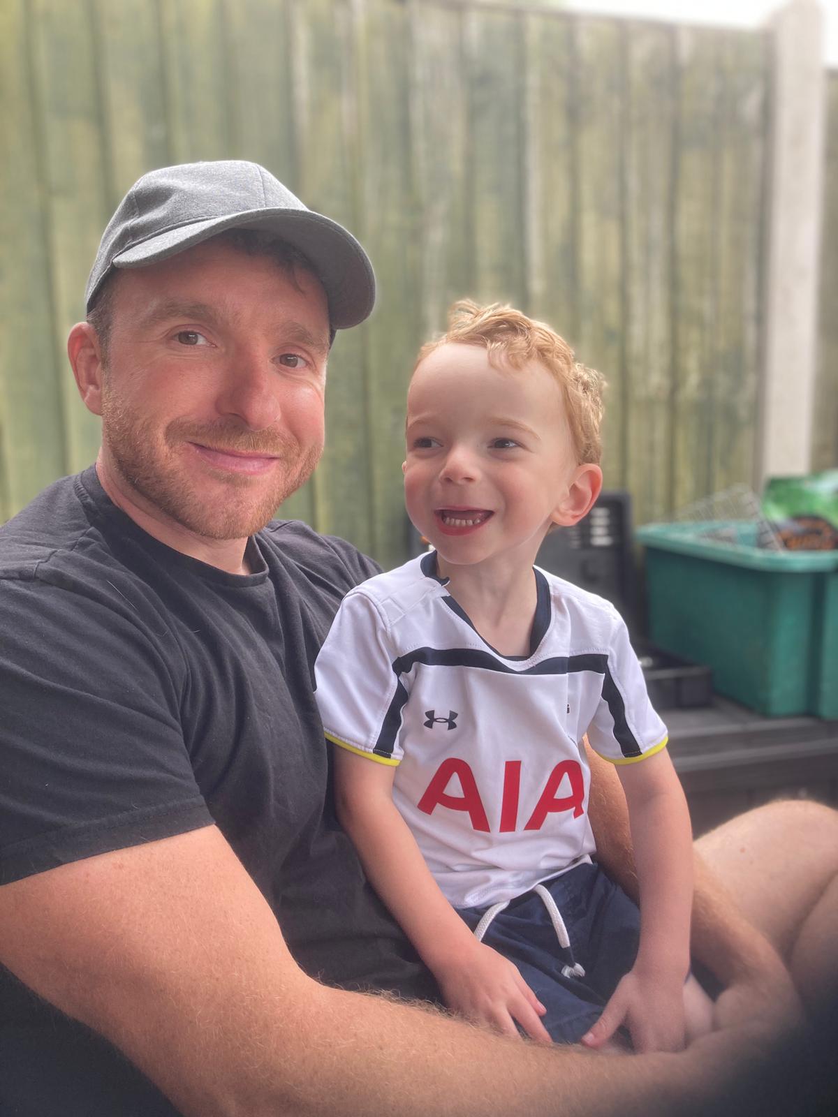 A man in a baseball cap sitting with his young son in a garden