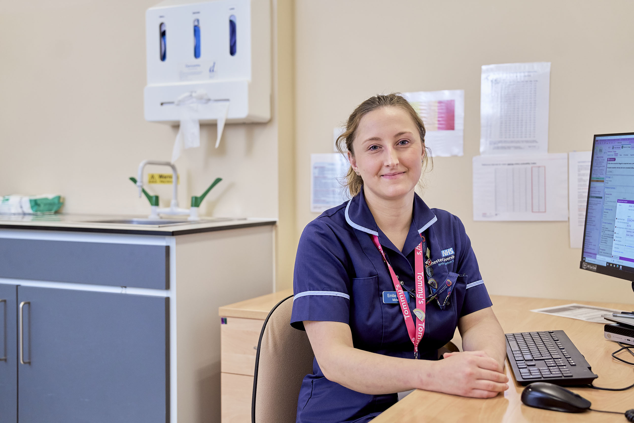 A Tommy's Rainbow Midwife sits at a desk smiling at the camera