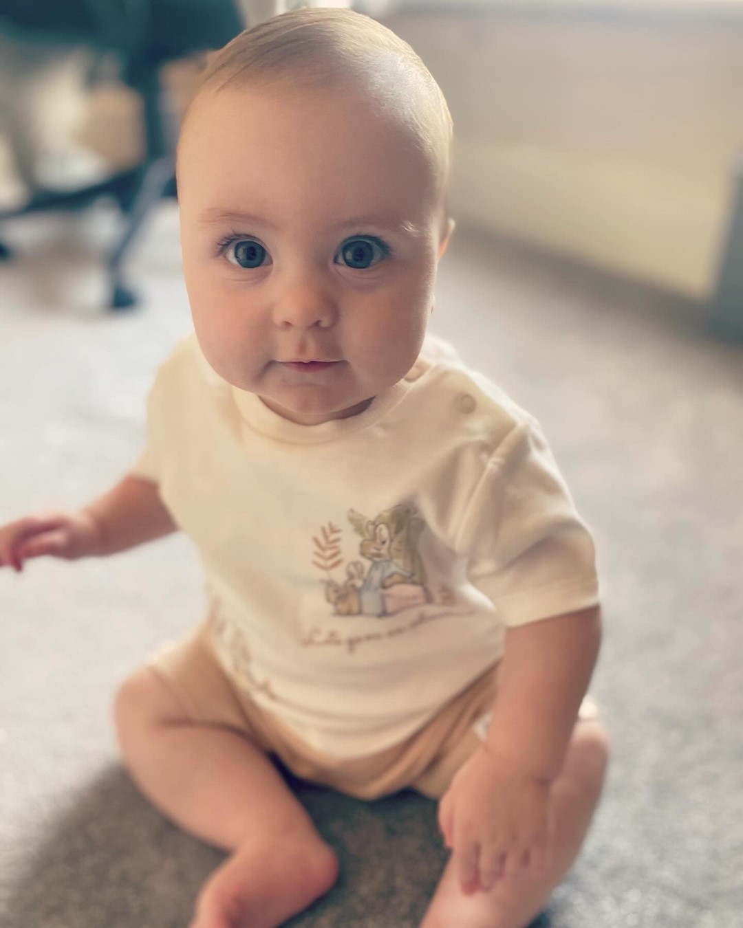 A baby boy sitting upright on a carpet and smiling