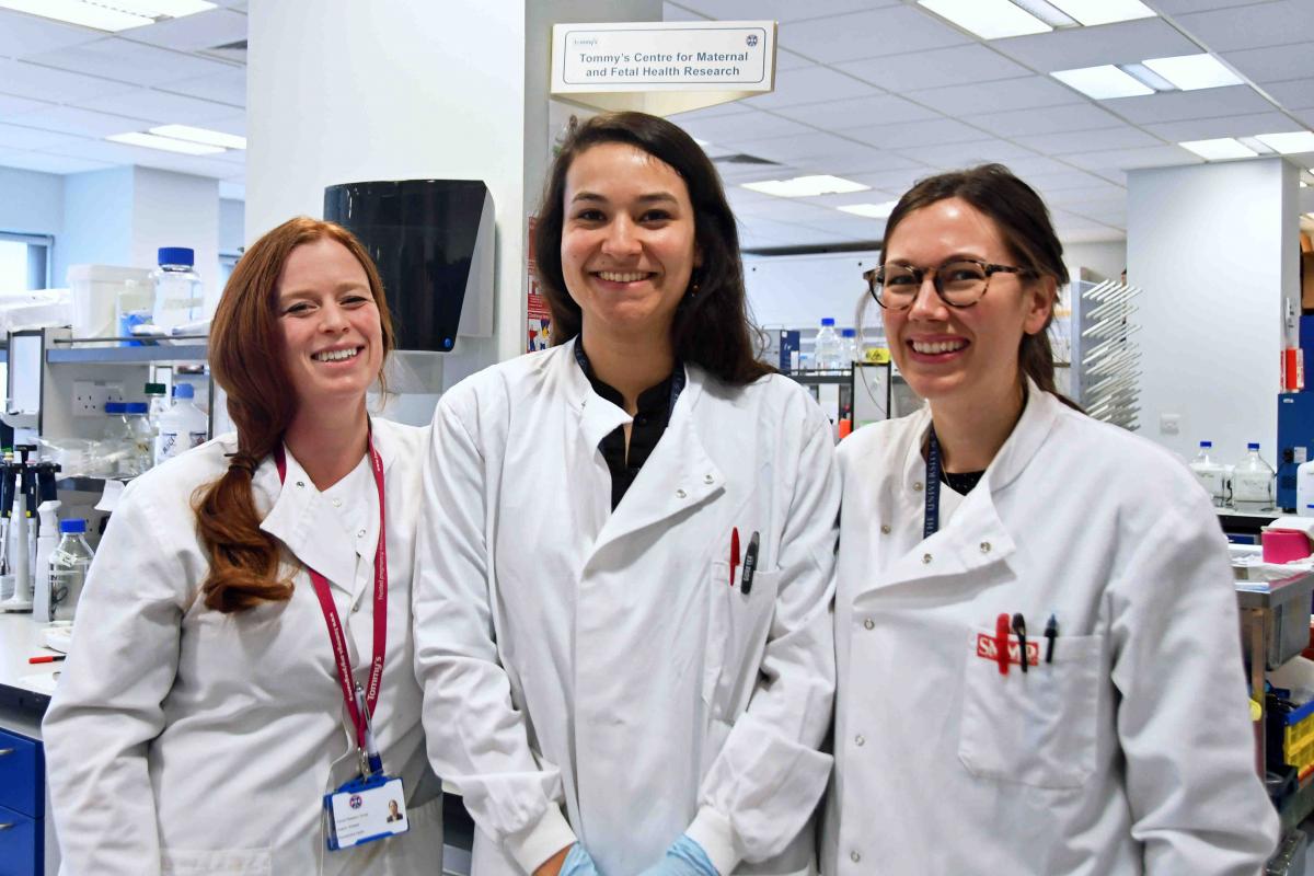 Three smiling female researchers wearing lab coats in a science lab