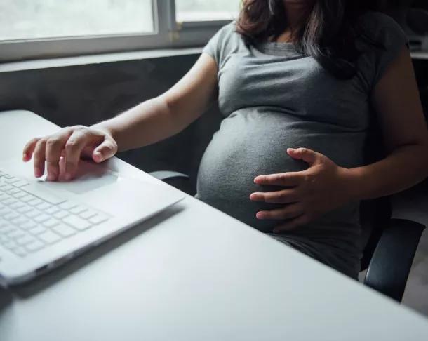 Image of pregnant lady with one hand on bump, on hand on keyboard