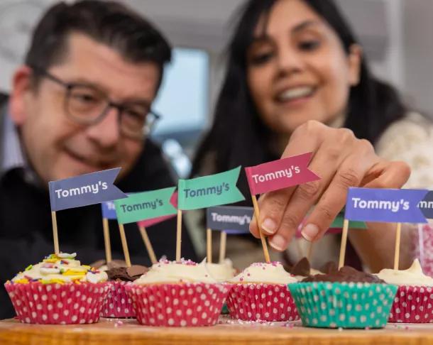 Two happy people displaying cupcakes with Tommy's cake flag decorations